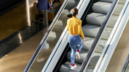 young man climbing up the escalator one step at a time with the help of the handrail, because they are without electricity and the sunlight is reflected on the stairs