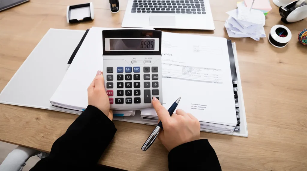 the person punching numbers into a calculator at a desk with a computer and manual.